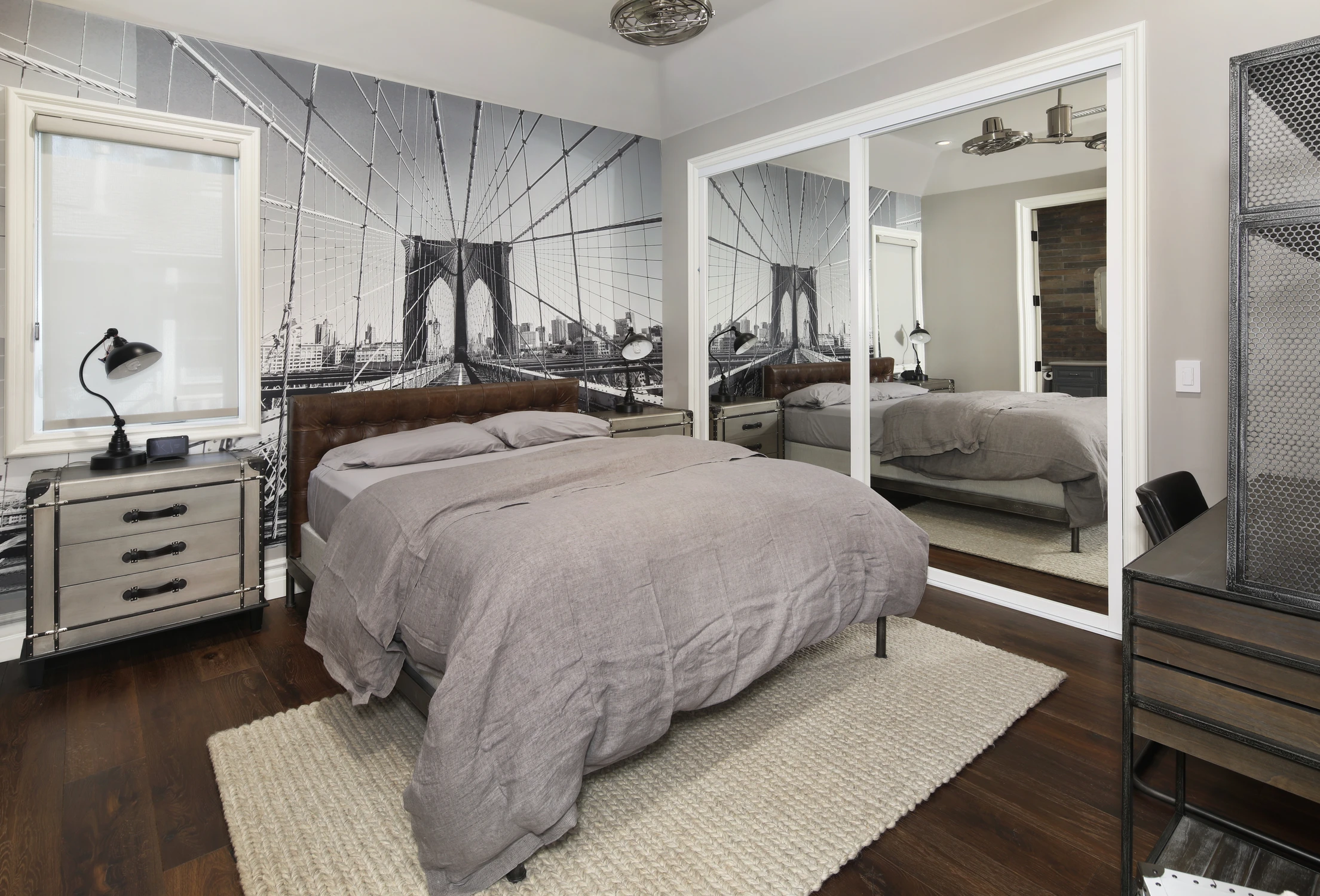 Bedroom with gray bedding, city mural wall, and mirrored closet panels